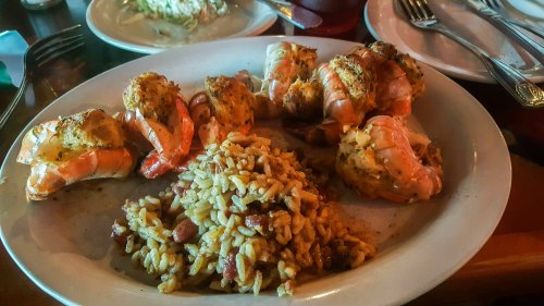 A plate featuring grilled shrimp seasoned with spices, served alongside a portion of rice and beans.