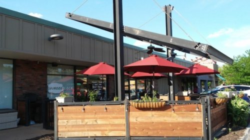 Outdoor dining area with red umbrellas, wooden fencing, and a modern building in the background under a clear blue sky.