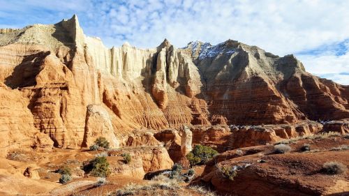 A stunning landscape of towering red rock formations and cliffs under a blue sky with scattered clouds.