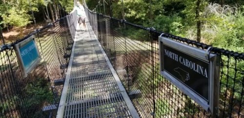 A suspension bridge in North Carolina surrounded by trees, with signs marking the state on either side.