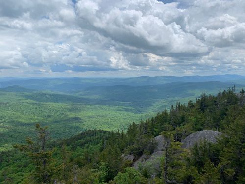 A panoramic view of lush green mountains under a cloudy sky, with rocky outcrops in the foreground.