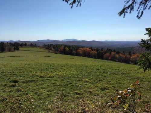 A scenic view of rolling hills and colorful autumn trees under a clear blue sky.