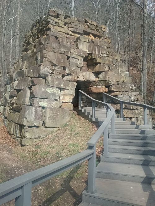 Stone structure with a large entrance, surrounded by trees and a wooden staircase leading up to it.