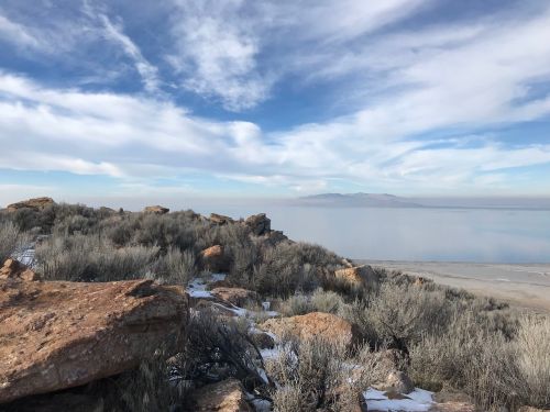A rocky landscape with sparse vegetation overlooking a calm body of water under a cloudy sky.