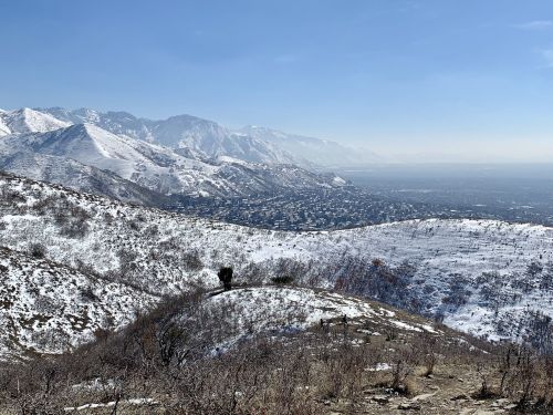 Snow-covered mountains overlook a valley, with a clear blue sky and distant peaks in the background.