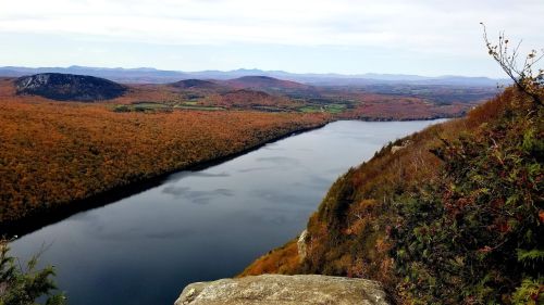 A scenic view of a river winding through vibrant autumn foliage and rolling hills under a cloudy sky.