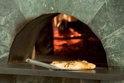 A freshly baked pizza on a peel, with a stone oven and glowing embers in the background.