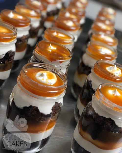 Rows of dessert jars filled with layers of chocolate, cream, and caramel, topped with a swirl of whipped cream.