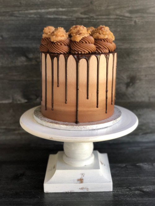 A beautifully decorated cake with chocolate drips, topped with swirls and cookie-like treats, displayed on a white pedestal.