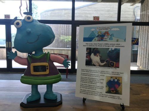 A colorful cartoon robot statue with a sign about its history and connection to Duke Power's 50th anniversary celebration.