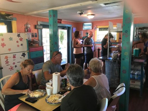 A cozy restaurant scene with diners enjoying meals at a table while others chat near the kitchen. Colorful decor surrounds them.