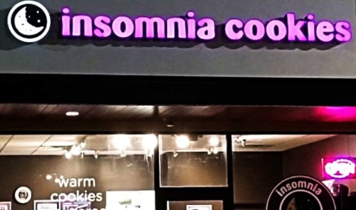 Sign for Insomnia Cookies, featuring a moon logo and text promoting warm cookies, illuminated at night.