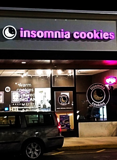 Exterior of Insomnia Cookies shop at night, featuring a sign with the logo and warm cookie offerings.