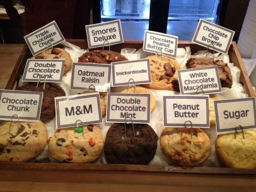 A tray of assorted cookies with labels, including flavors like S'mores Deluxe, Oatmeal Raisin, and Peanut Butter.