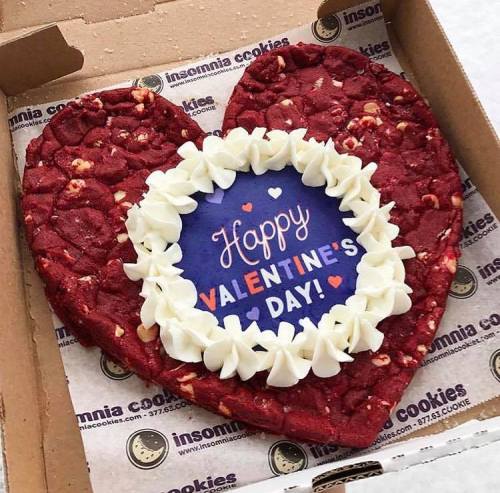 A heart-shaped red velvet cookie with white frosting and a "Happy Valentine's Day!" sign in the center, in a box.