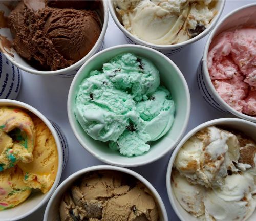 A variety of ice cream flavors in cups, including mint, chocolate, vanilla, and strawberry, arranged in a circle.