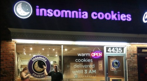 A storefront of Insomnia Cookies, featuring a sign that says "warm cookies delivered until 3 AM."
