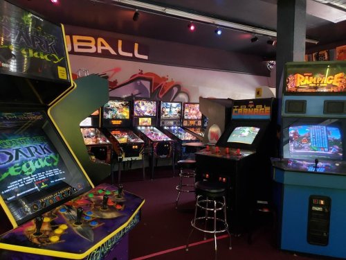 A vibrant arcade filled with various pinball machines and classic video game cabinets in a colorful setting.