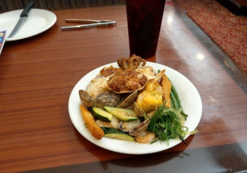 A plate of seafood with vegetables, including clams, green beans, and a fried item, next to a drink on a wooden table.