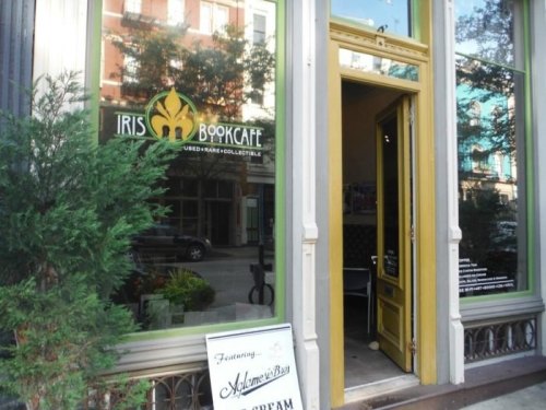 Entrance of Iris Bookcafe, featuring a sign and greenery outside, with a view of the interior through the door.