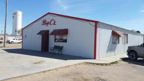 A white metal building with a red roof and signage reading "Big C's," featuring a bench outside and a clear blue sky.