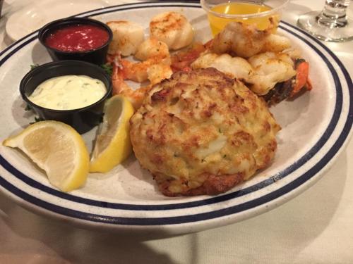 A plate of seafood featuring scallops, shrimp, a crab cake, lemon wedges, and dipping sauces.