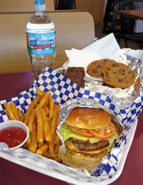 A tray with a burger, fries, a bottle of water, cookies, and a brownie, all served on a checkered paper.