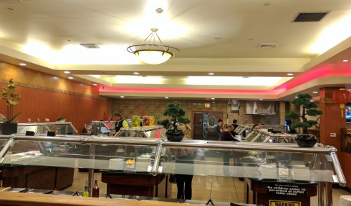 A buffet restaurant interior with food stations, diners, and staff serving in a warm, inviting atmosphere.