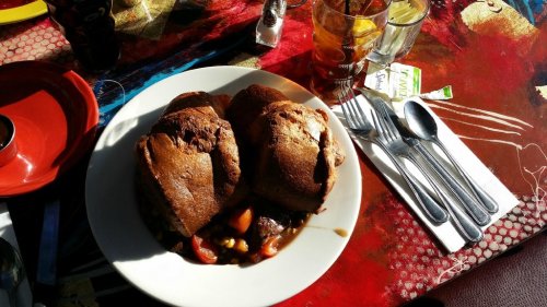 A plate of two large, stuffed pastries on a colorful table, accompanied by utensils and drinks in the background.