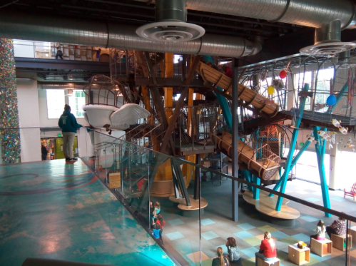 A colorful indoor play area featuring slides, climbing structures, and children playing in a vibrant, spacious environment.