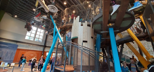 A colorful indoor play structure with climbing features, surrounded by children and families in a lively space.