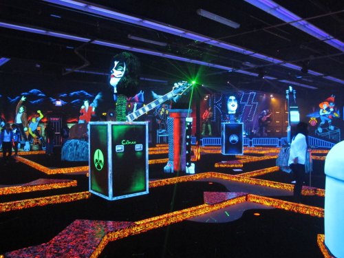 A vibrant glow-in-the-dark mini-golf course featuring rock-themed decorations and colorful lighting effects.