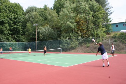 A group of people playing tennis on an outdoor court surrounded by trees.