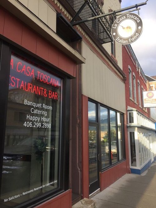 Exterior view of La Casa Toscana, an Italian restaurant, featuring a sign with contact info and happy hour details.