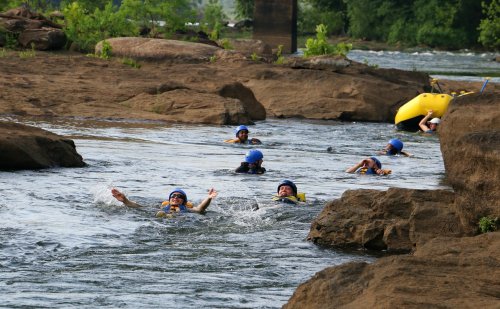A group of people in helmets and life jackets floating in a river, surrounded by rocks and greenery.