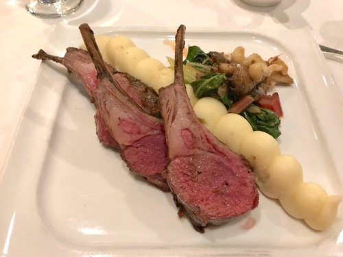 Three lamb chops served with creamy potato purée and sautéed greens on a white plate.