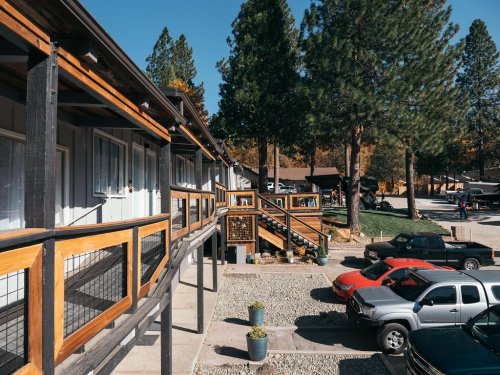 A view of a lodge with wooden balconies, surrounded by trees and parked cars in a sunny outdoor setting.