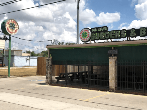Exterior of Big Lou's Burgers & BBQ, featuring a green sign and outdoor seating area under a cloudy sky.
