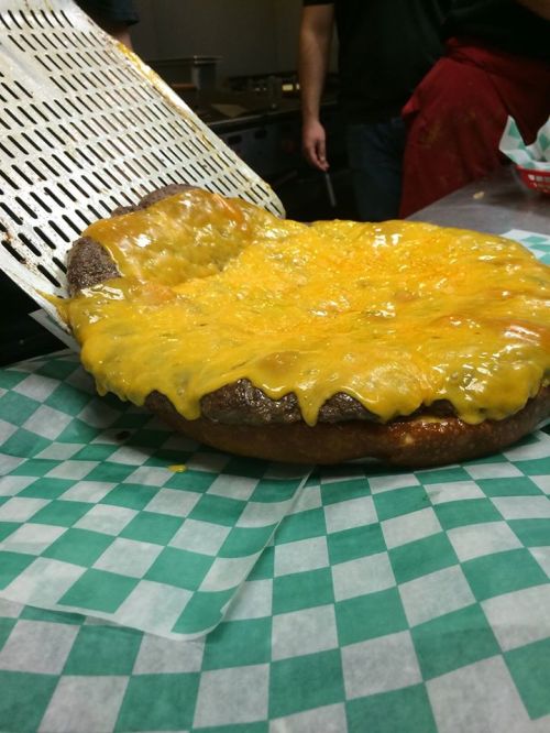 A large, cheesy pizza with melted cheddar cheese, resting on a green and white checkered paper.