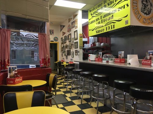 A retro diner interior with yellow and black decor, checkered floor, and red accents, featuring booths and a counter.