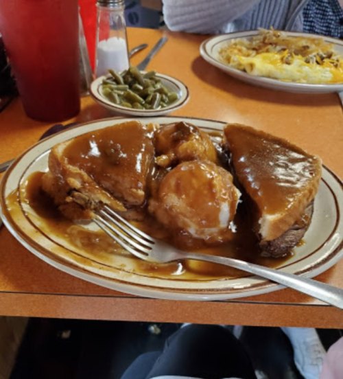 A plate of meat with gravy, mashed potatoes, and green beans on a table in a diner setting.