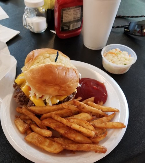 A plate with a cheeseburger, fries, ketchup, and a side of coleslaw on a black table.