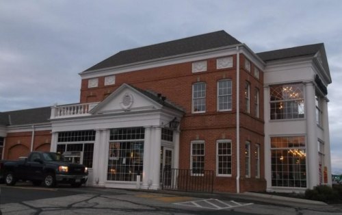 A brick building with large windows and a white entrance, featuring a truck parked in front.