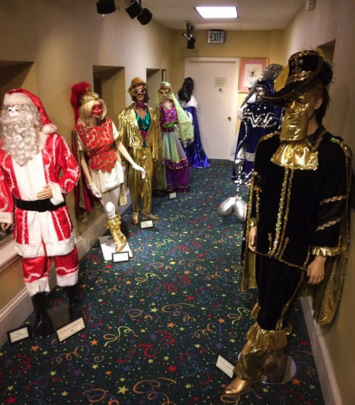 A hallway lined with mannequins in various colorful costumes, including a Santa suit and glamorous outfits.