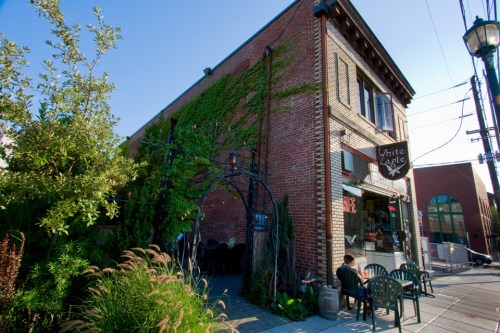 A brick building covered in greenery, featuring a café sign, outdoor seating, and a clear blue sky.