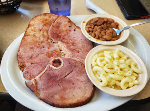 A plate with a large slice of ham, macaroni and cheese, and baked beans on the side.