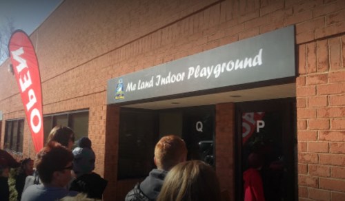 Entrance to "Me Land Indoor Playground" with a red "Open" flag and a line of people waiting outside.