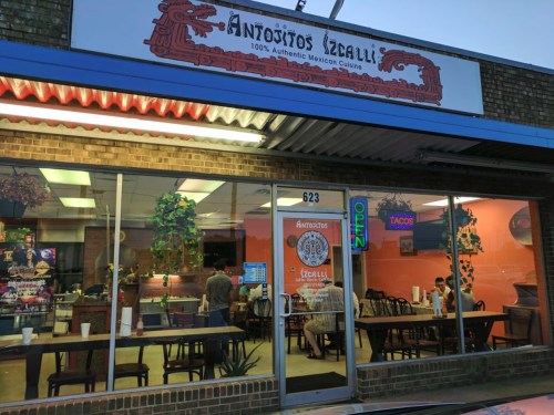 Exterior of Antojitos Izcalli, a Mexican restaurant, featuring an open sign and a cozy dining area visible through the windows.