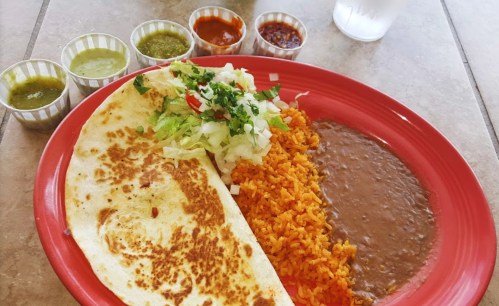 A plate of food featuring a large tortilla, rice, refried beans, and various colorful salsas in small cups.