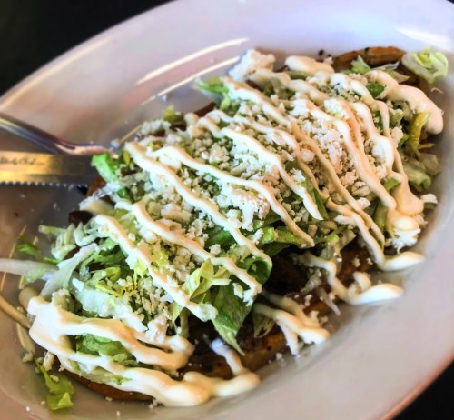 A plate of tacos topped with lettuce, cheese, and drizzled with creamy sauce.
